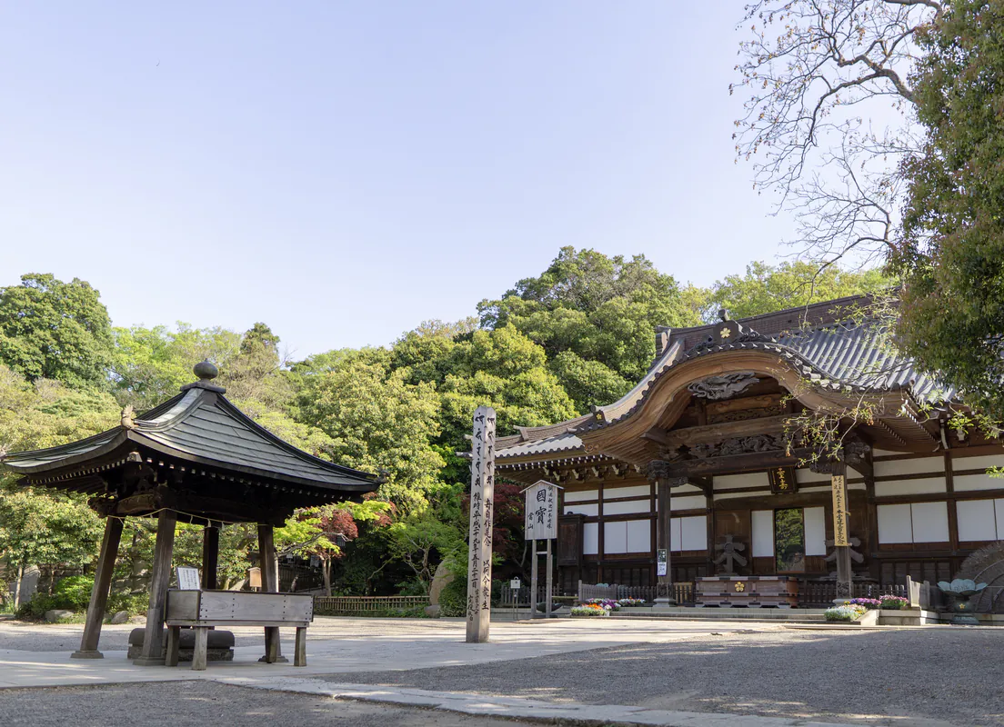 寺院の境内。大きな木の堂と、四本柱の屋根、砂利の広場
